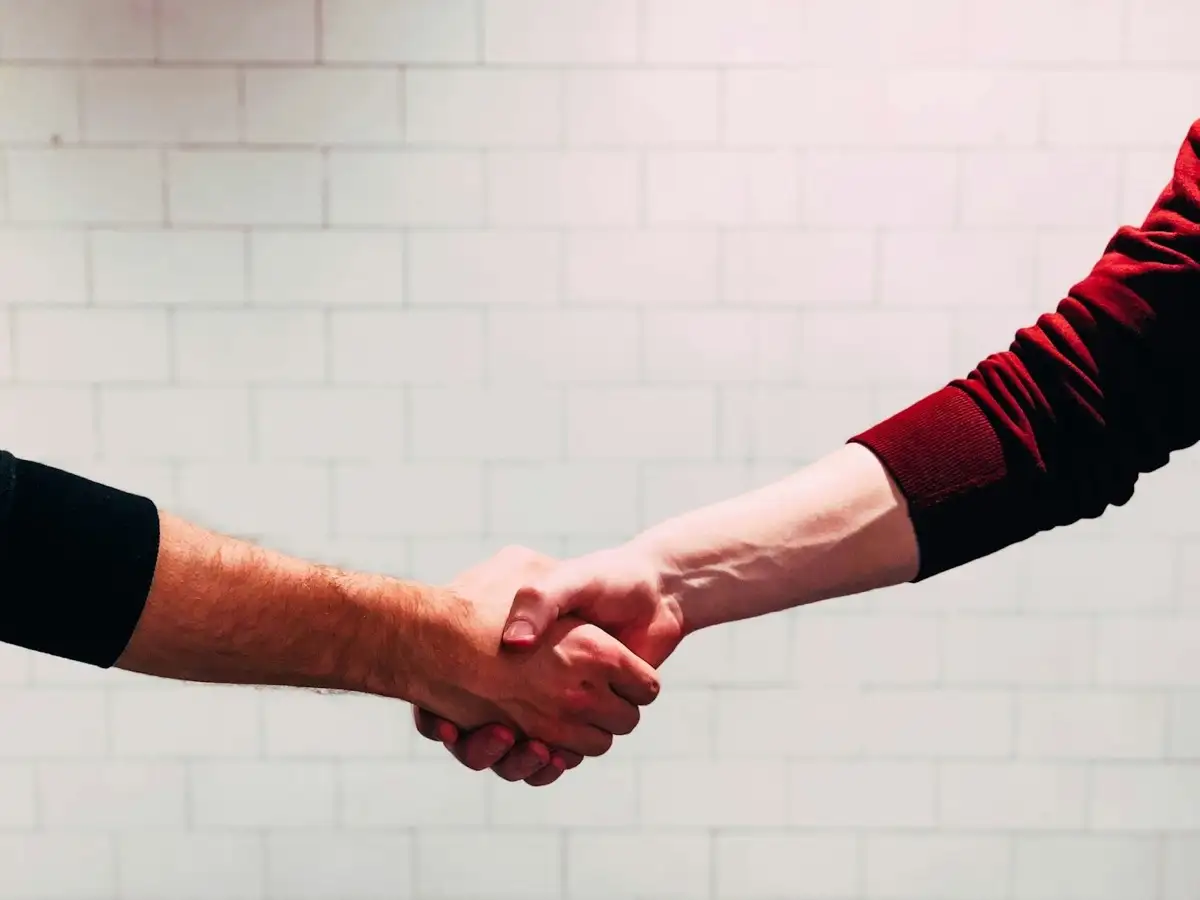 Two people shaking hands near a white wall