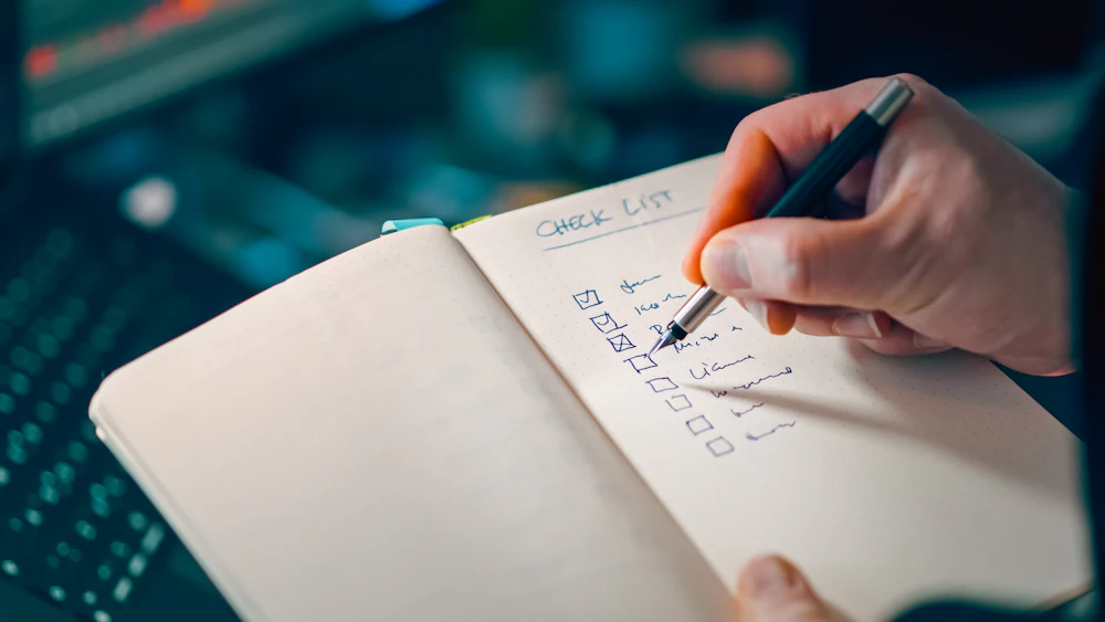 A checklist being written on a notepad, representing what to compare before choosing a breakup coaching plan