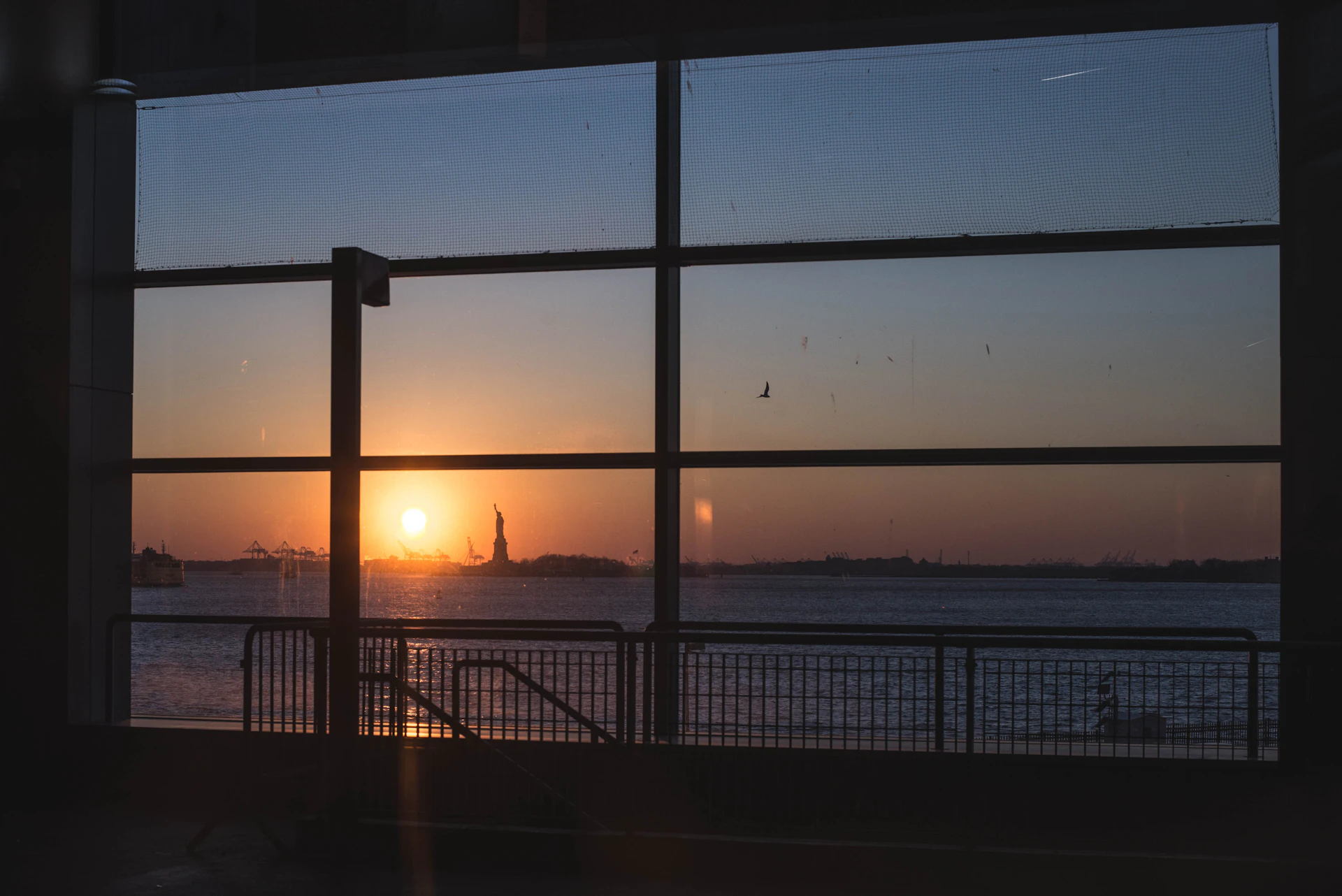 Sunrise over New York Harbor and the Statue of Liberty, seen through a window — a quiet moment looking toward what comes next