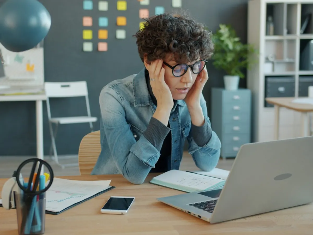 A man at a desk with his hands in his hair, looking at a laptop