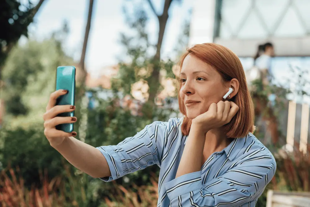 Young woman wearing an earbud smiling during a video call outdoors