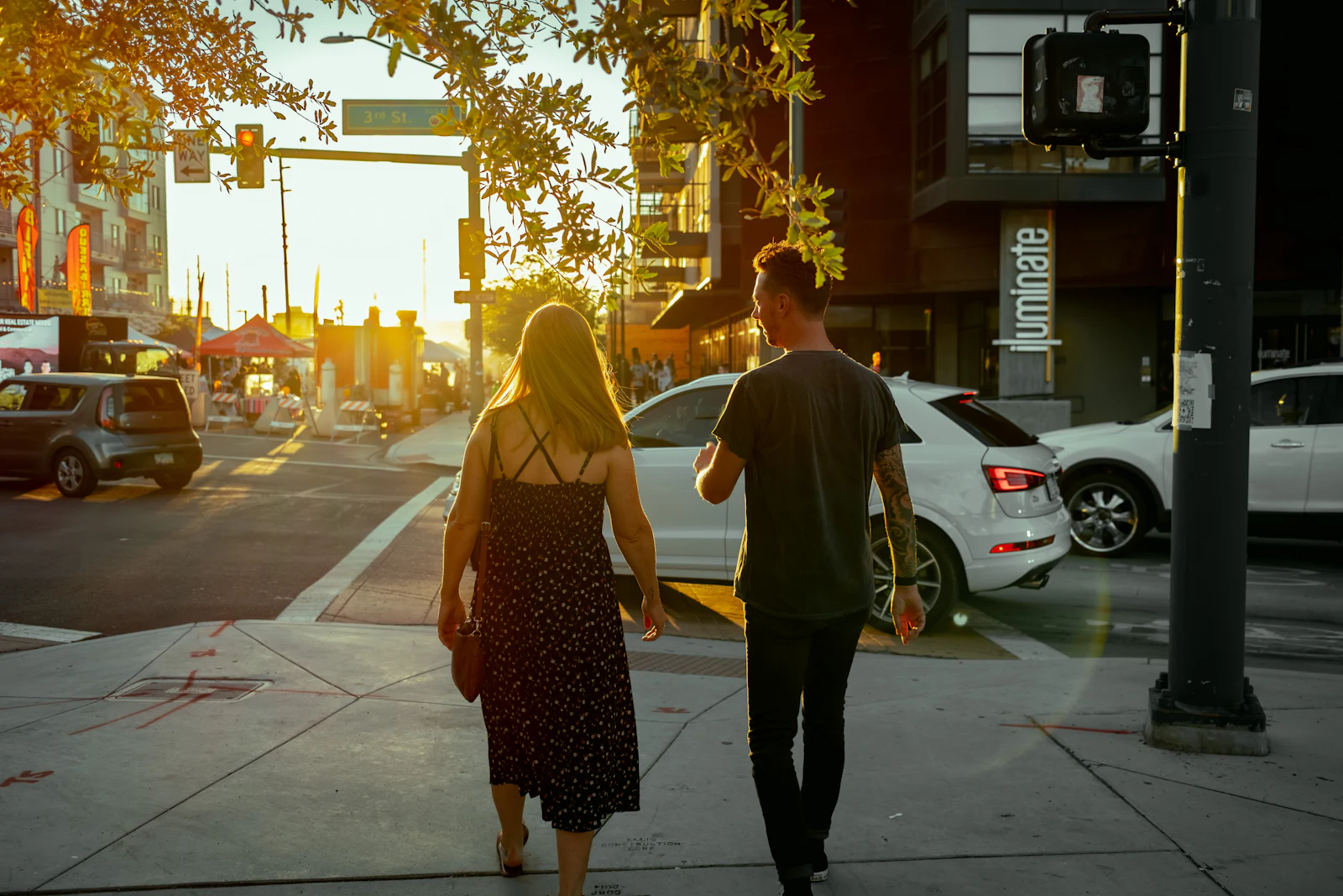 A man and a woman walking down a city street in golden evening light, seen from behind