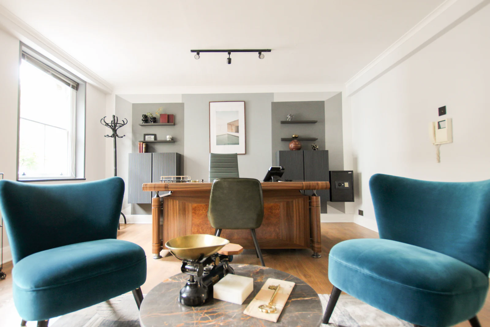 A calm consulting room with two blue armchairs and a wooden desk
