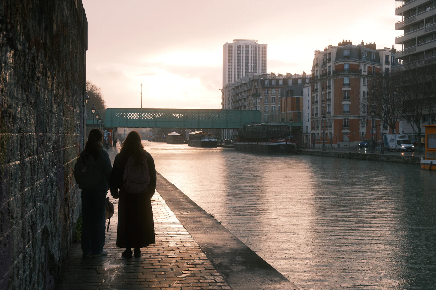 Two people walking together along a canal at sunset, seen from behind