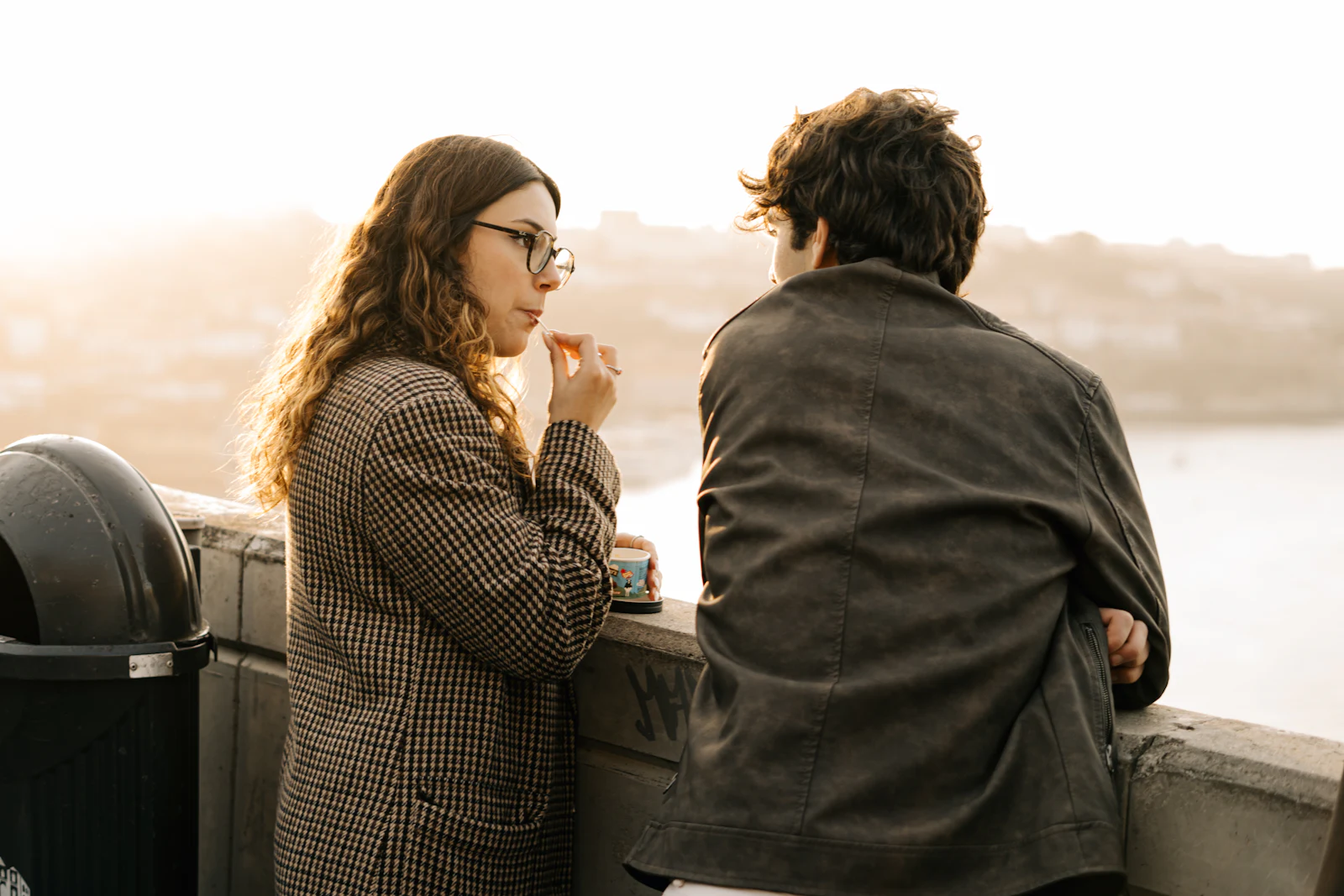 A woman and a man leaning on a railing by the water, talking quietly