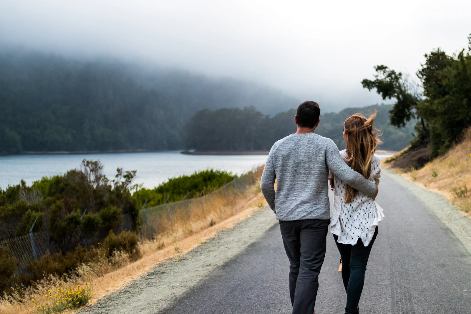 A couple walking side by side along a quiet lakeside road