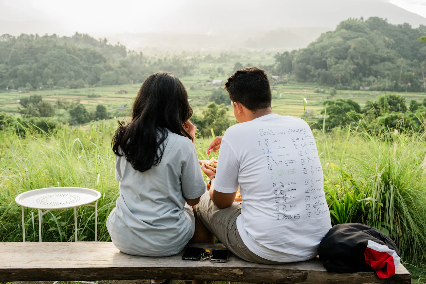 Two people sitting together on a ledge, looking out at green hills
