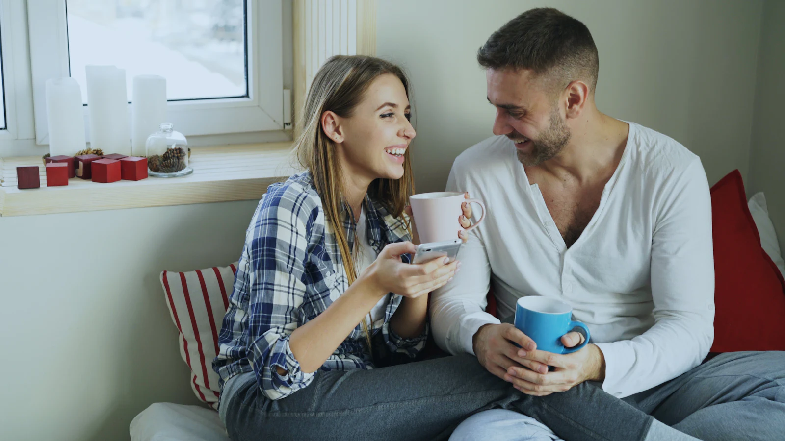 A couple laughing over coffee on a sofa by a window