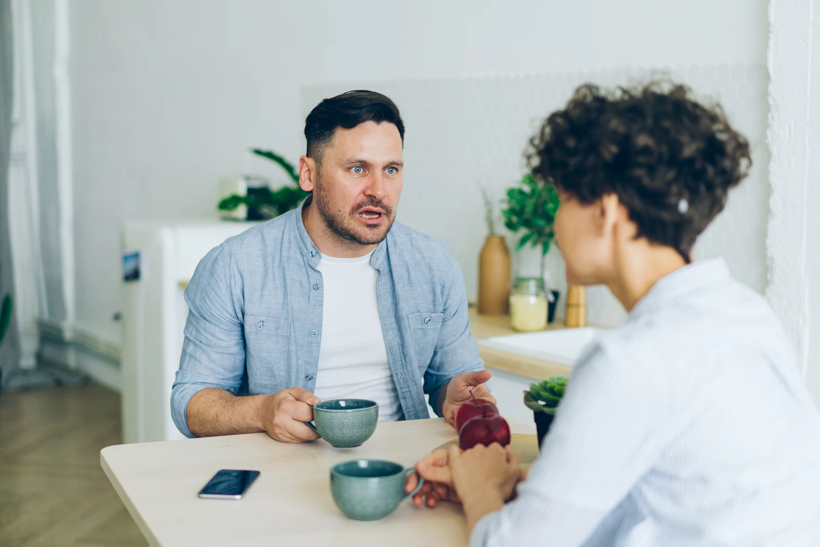 A man and a woman talking across a table in a bright room