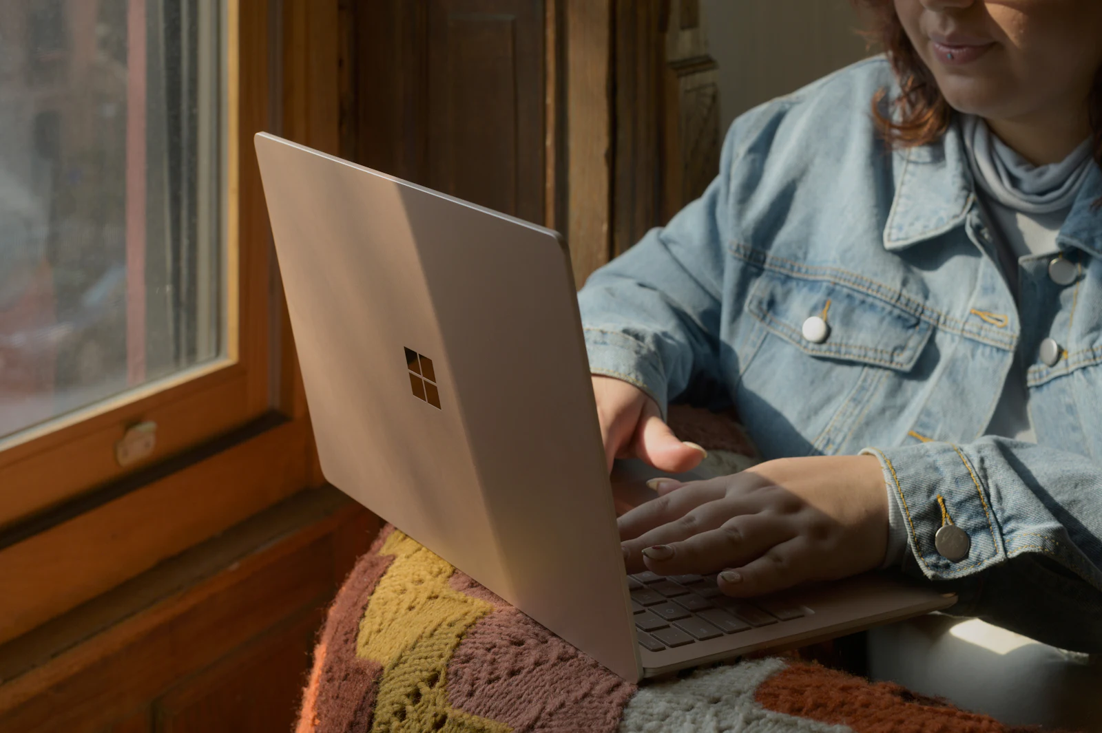 A woman using a laptop in a chair by a sunlit window