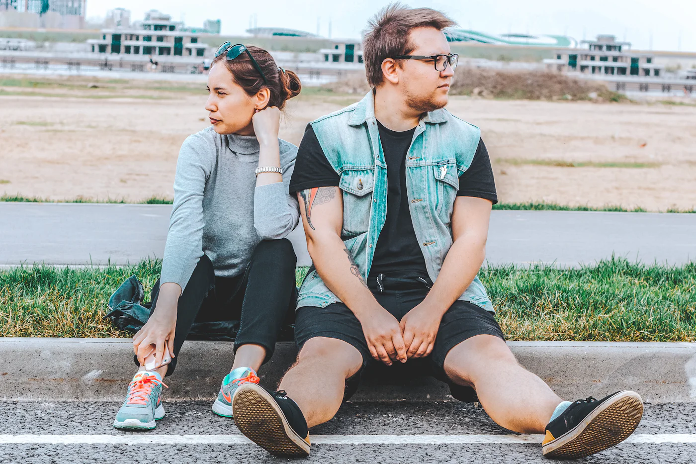 A woman and a man sitting on a curb, looking in different directions