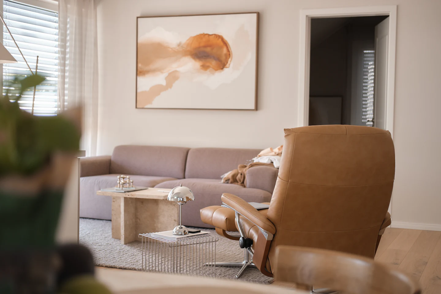 A sunlit living room with a sofa, a coffee table and a leather recliner
