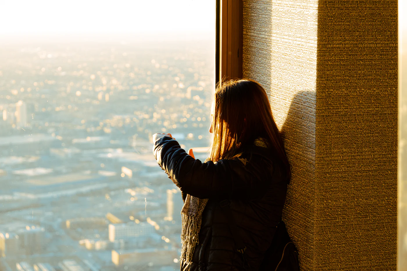 A woman standing at a window, looking out over a city in golden light